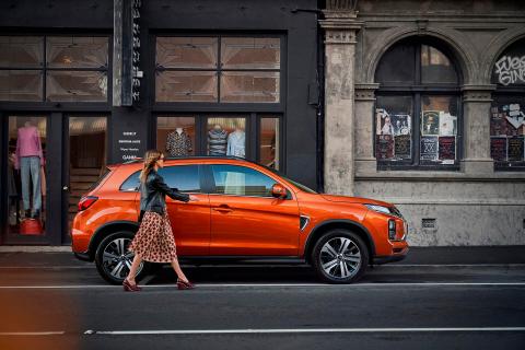 A women walk passing an orange Mitsubishi ASX parking front of a old building