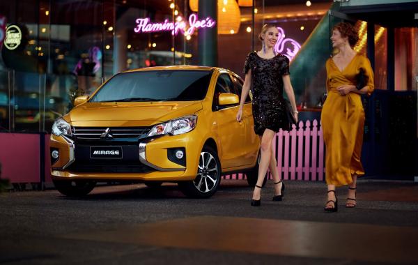 Two nicelydressed females walking past a Mitsubishi Mirage outside a bar at night